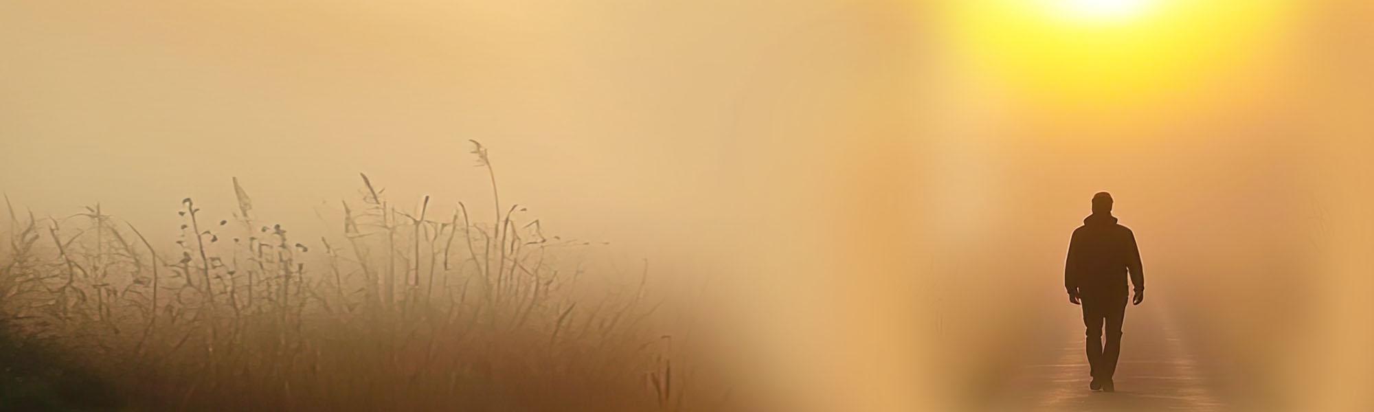Man walking on road toward sun