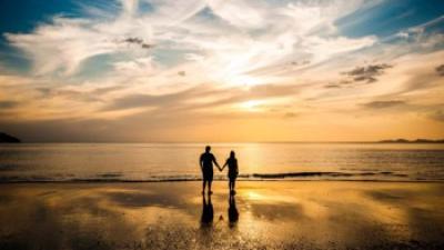 Two people holding hands near the ocean sunset