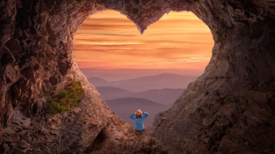 Woman sitting on heart shaped rock formation looking at the sunset
